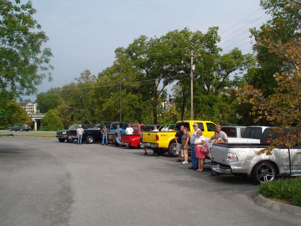Several pickup trucks parked in a lot with people standing around them. The trucks appear to be from the late 1990s