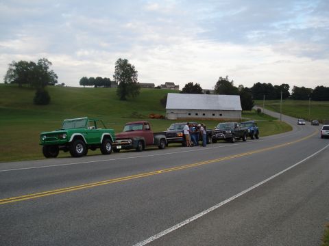 1994 Ford F-350 - Several classic trucks and SUVs are lined up on the shoulder of a country road next to a large barn.