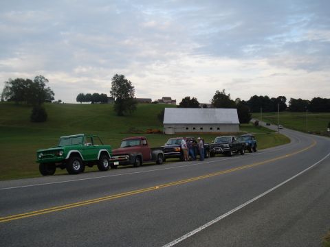 1994 Ford F-350 - A line of classic Ford trucks and SUVs are parked along a rural road with a barn in the background.
