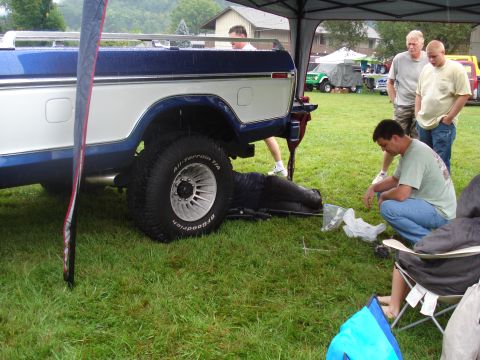 1994 Ford F-350 - A man works on the rear wheel of a lifted Ford F-Series truck at an outdoor event.