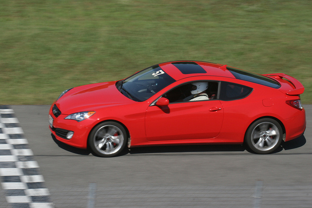Red 2010 Hyundai Genesis coupe on a racetrack with a racing number on the windshield
