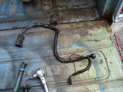 1994 Ford F-350 - A close-up view of a damaged wiring harness and a ratchet lying on the rusty floor of a truck bed.