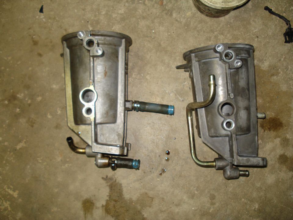 Two automotive fuel filters with metal and rubber hoses attached, lying on a concrete floor