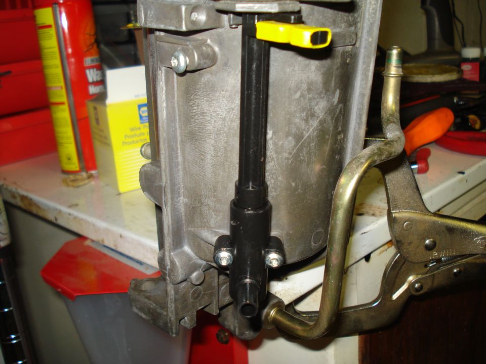 Engine part held by vise grips, with yellow lever and metal tube attached
