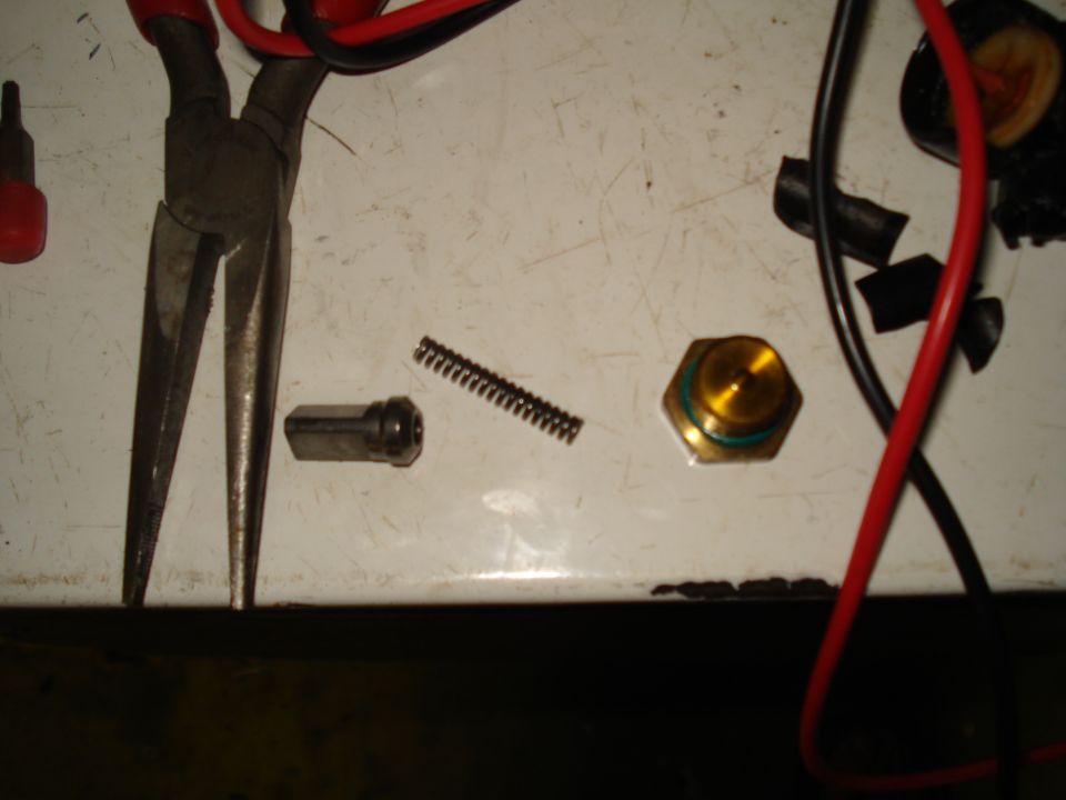 Pliers, a spring, a metal cylinder, and a brass sensor with green o-rings on a white surface