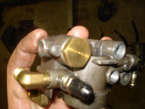 1994 Ford F-350 - A metal fuel filter housing with brass fittings is held in a dirty hand, with other engine parts in the background.