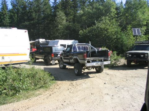 1986 Ford Bronco - Several off-road vehicles and an RV are parked on a dirt path surrounded by trees.