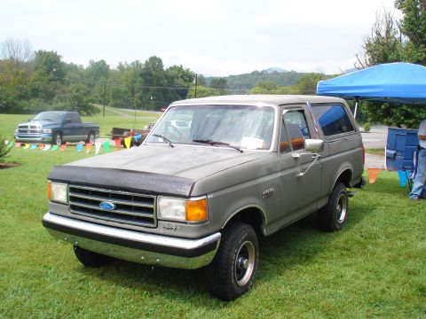 1994 Ford F-350 - A gray Ford Bronco is parked on a grassy field, with a blue Dodge Ram pickup visible behind it.