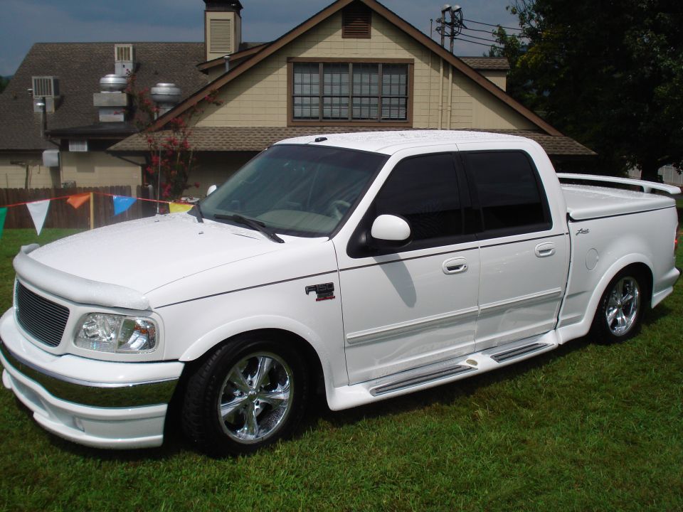 White pickup truck with custom body kit and chrome wheels parked on grass
