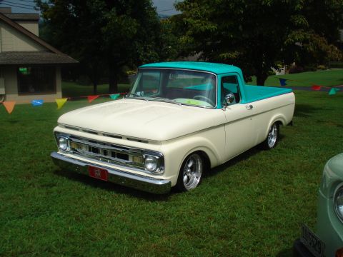1994 Ford F-350 - A classic cream and teal Ford pickup truck is displayed on a grassy lawn with colorful flags in the background.