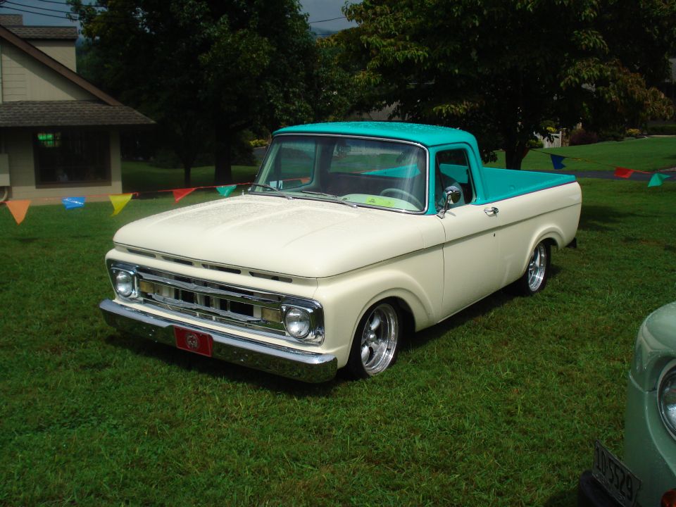 Cream and teal 1965 Ford F-100 pickup truck with chrome bumper and aftermarket wheels, parked on grass