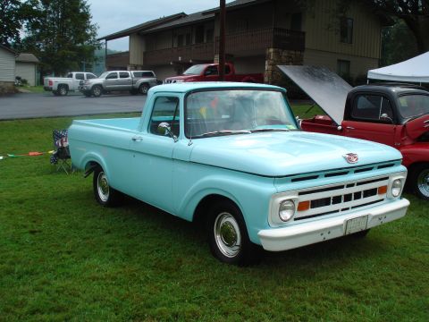 1994 Ford F-350 - A classic light blue pickup truck is parked on a grassy lawn with other vehicles and a building visible.