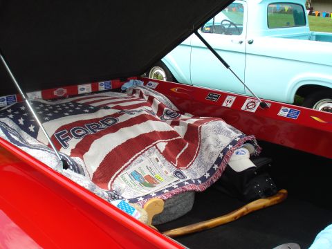 1994 Ford F-350 - The bed of a red pickup truck is covered with an American flag blanket, with a light blue 1956 Ford F-100 visible behind it.