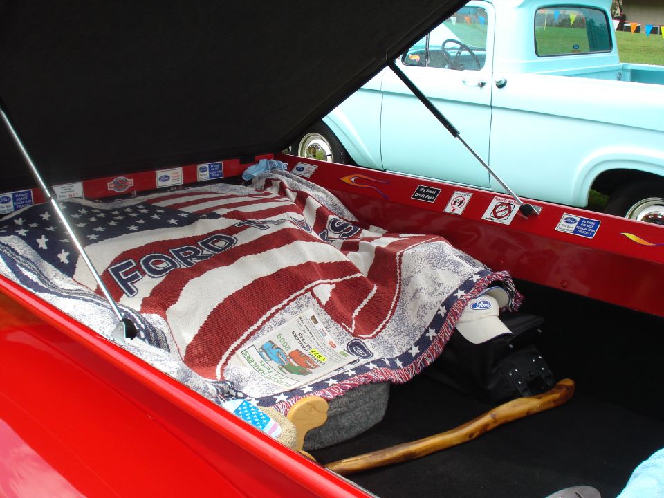 Red pickup truck bed with an American flag blanket and a light blue 1956 Ford F-100 in the background