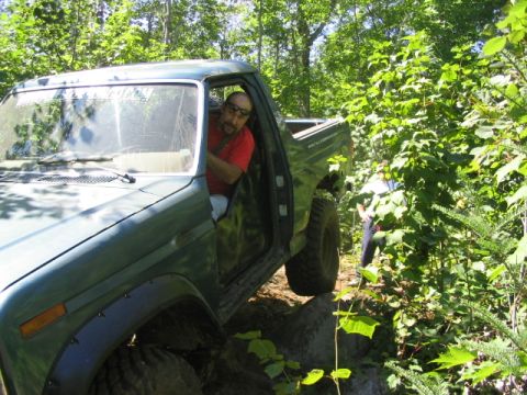 1986 Ford Bronco - A man in a red shirt drives a green SUV through a rocky, wooded area.