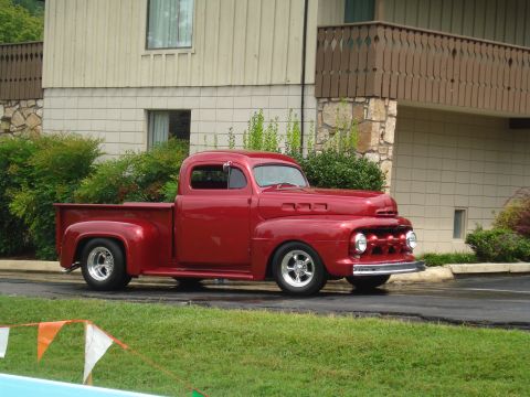 1994 Ford F-350 - A red classic pickup truck is parked on asphalt in front of a building with greenery.