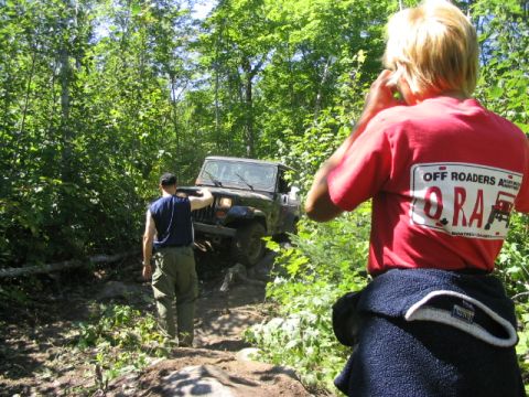 1986 Ford Bronco - A Jeep navigates a challenging off-road path in a dense forest environment.