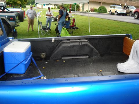 1994 Ford F-350 - The bed of a blue pickup truck contains a cooler and a tarp, with people and other vehicles visible in the background.