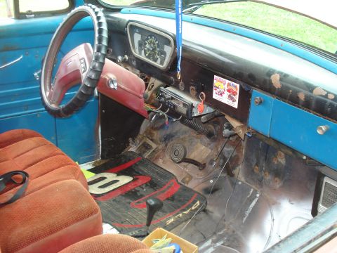 1994 Ford F-350 - The interior of a blue truck features orange seats, a worn dashboard, and a floor mat with racing graphics.