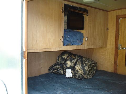 1994 Ford F-350 - The interior of a camper shows a bed with sleeping bags and cabinets containing a microwave and blankets.