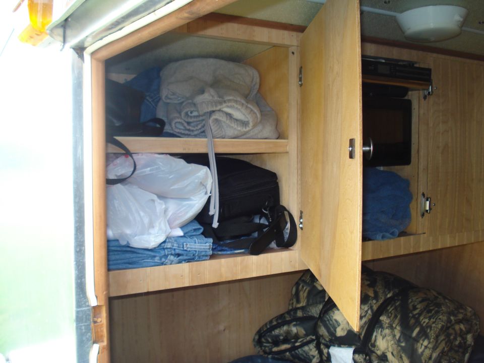 Interior view of open wooden cabinets filled with clothes and bags. A microwave is visible in a separate compartment