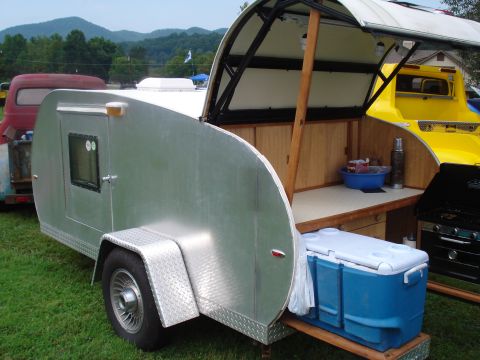 1994 Ford F-350 - A teardrop trailer is set up with an outdoor kitchen, parked alongside other vehicles on a grassy area.