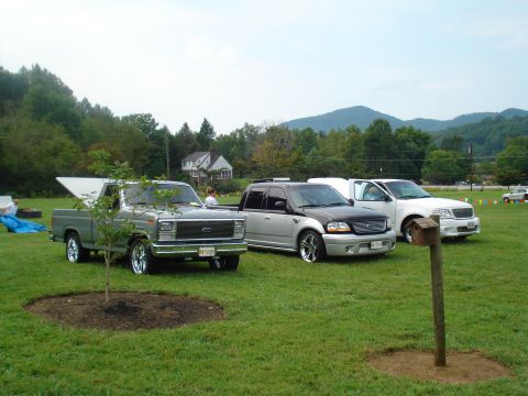 1994 Ford F-350 - Three trucks are parked on a grassy field with trees and hills in the background.