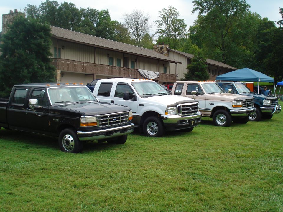 Four Ford F-Series trucks parked on grass in front of a building. The trucks appear to be from the late 90s