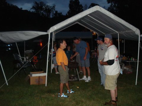 1994 Ford F-350 - People socialize under tents during an evening gathering, with a grill in the foreground.