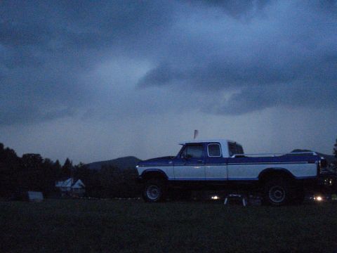 1994 Ford F-350 - A blue and white pickup truck is parked in a grassy field under a cloudy sky.