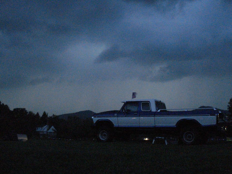 Blue and white pickup truck parked in a field under a cloudy sky