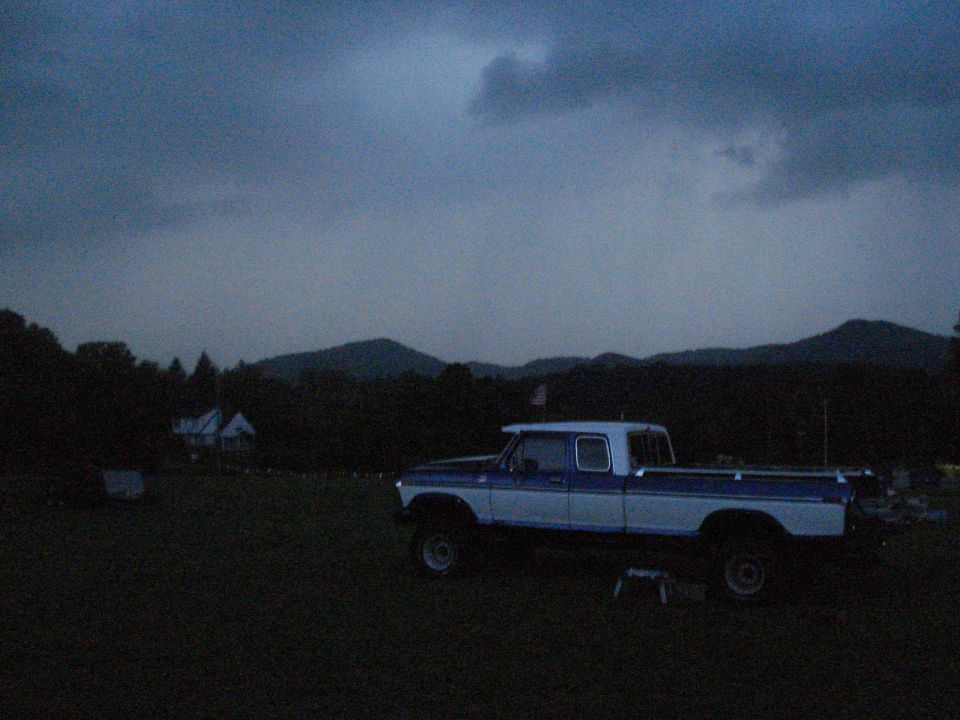 Blue and white pickup truck parked in a grassy field with hills in the background