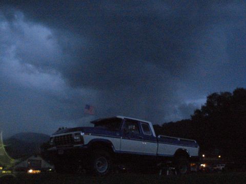 1994 Ford F-350 - A two-tone pickup truck sits under a dramatic, cloudy sky, with an American flag visible.
