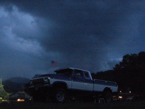 1994 Ford F-350 - A lifted Ford F-Series pickup truck sits under a stormy sky with an American flag in the background.