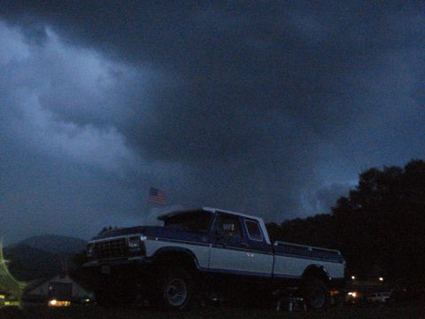 1994 Ford F-350 - A two-tone pickup truck sits under a dramatic, cloudy sky with an American flag visible.