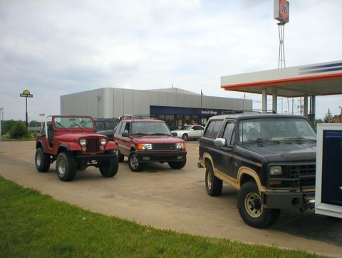 1983 Ford Bronco - A black 1983 Ford Bronco with tan trim is parked at a gas station next to a red Jeep and a red Range Rover.