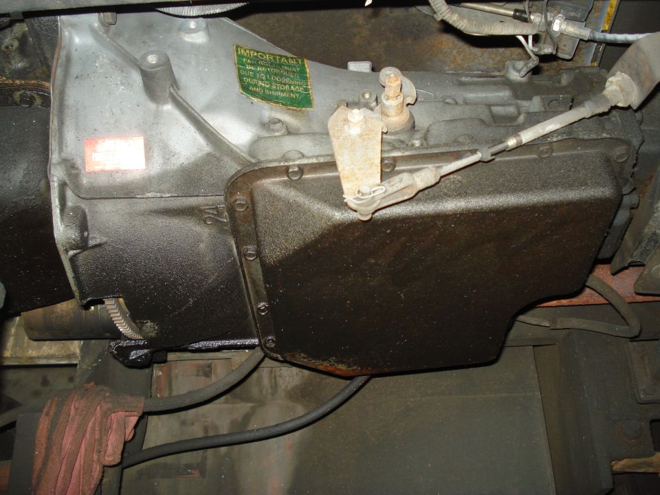 Transmission pan with linkage and an 'IMPORTANT' sticker. Numbers '24' are visible on the casing