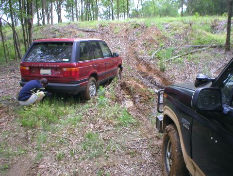1983 Ford Bronco - Two off-road vehicles navigate a muddy trail; one Range Rover appears stuck.