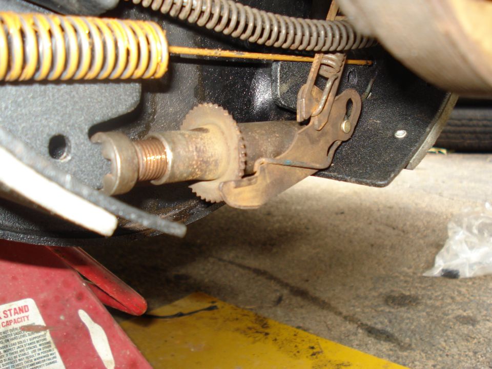 Close-up of a rusty parking brake mechanism with a yellow spring and a red jack stand