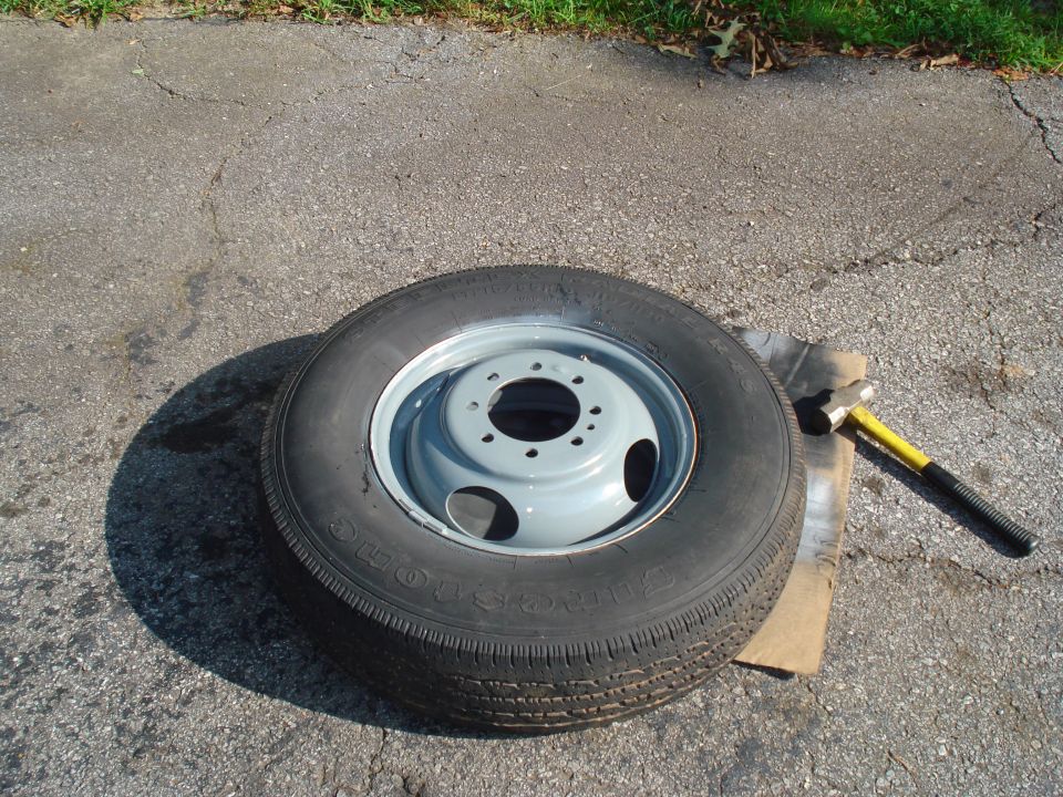 Spare tire with a dual rear wheel rim, lying on asphalt next to a hammer