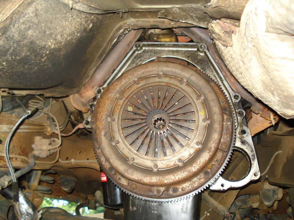 Underside view of a vehicle's clutch and transmission assembly. Shows the flywheel and pressure plate