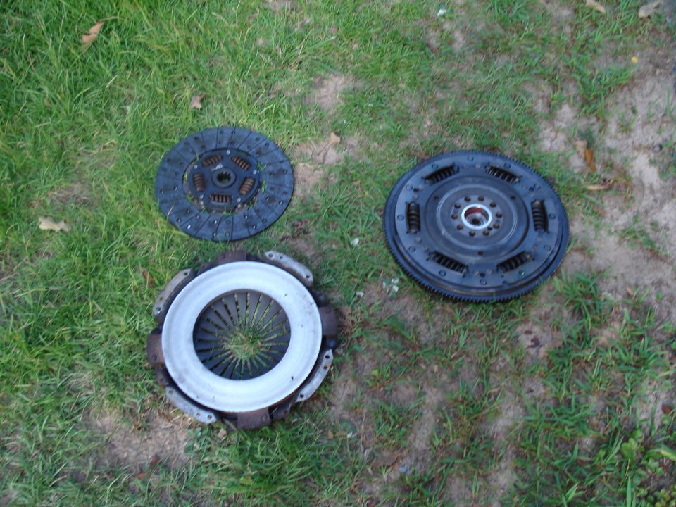 Clutch disc, pressure plate, and flywheel laid out on grass