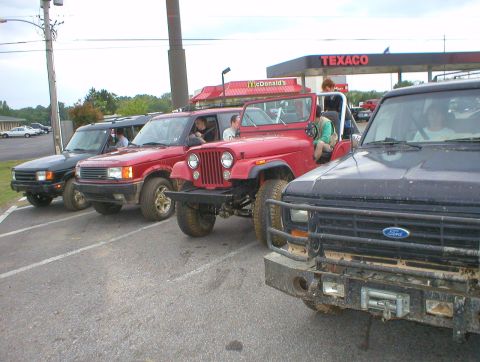 1983 Ford Bronco - Several off-road vehicles are parked in a line at a gas station.