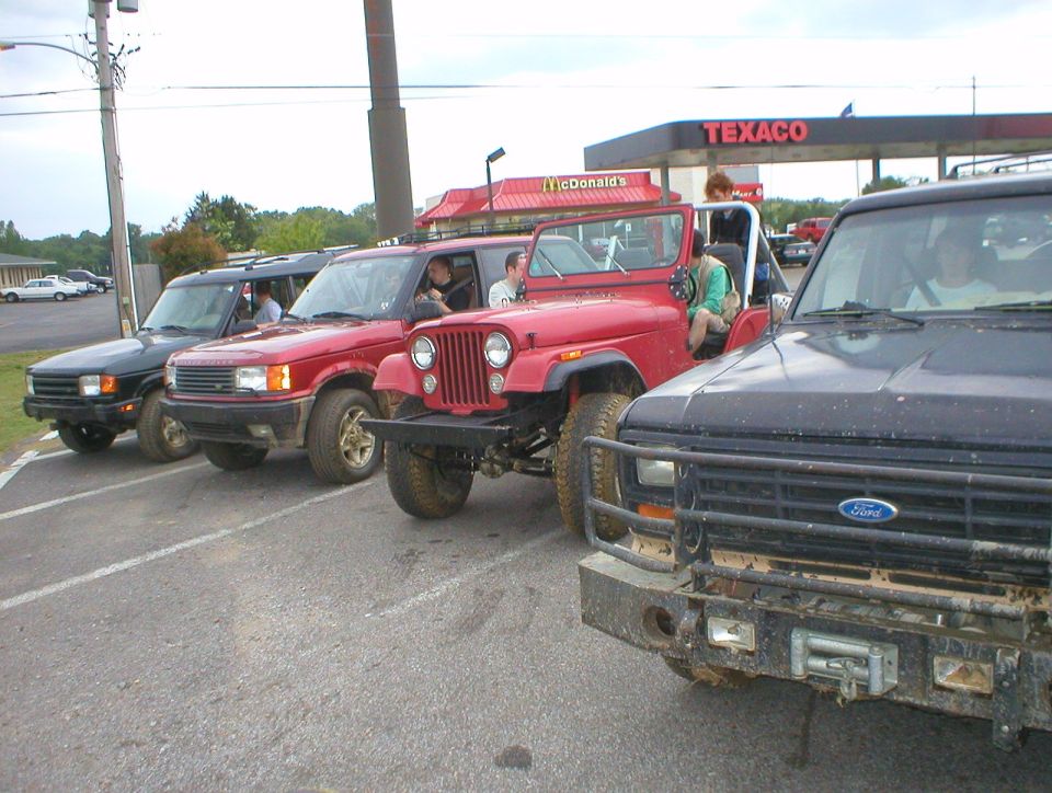 Dark Ford pickup front angle with brush bumper, parked by red Jeep and Land Rover at Texaco