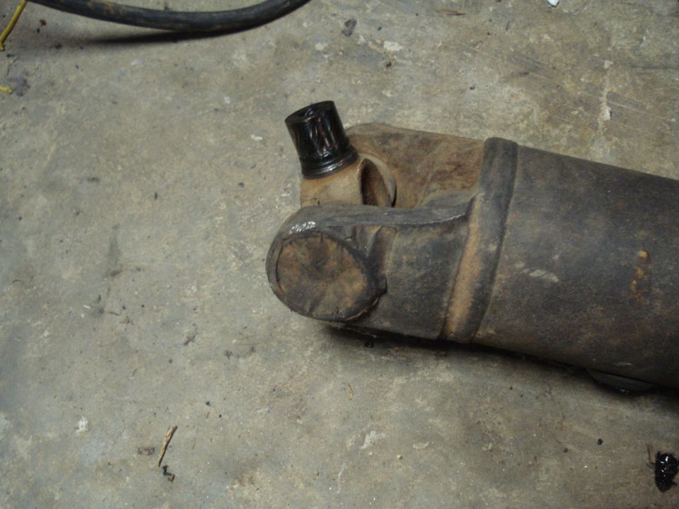 Close-up of a driveshaft U-joint and yoke, resting on a concrete floor