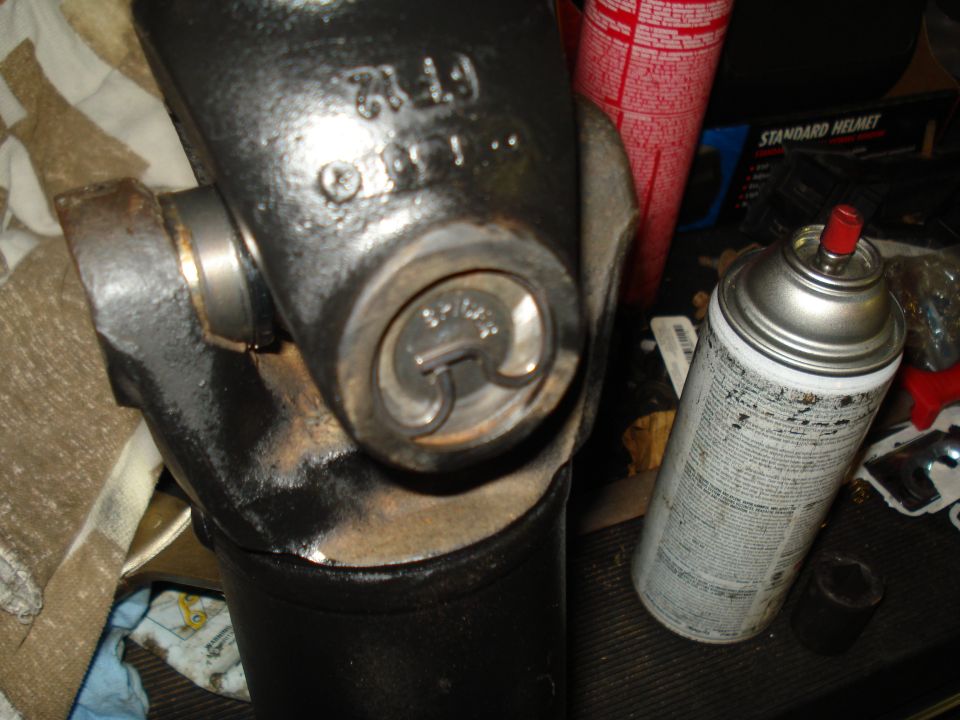 Black driveshaft universal joint with visible part numbers and a spray can nearby