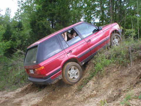 1983 Ford Bronco - A red Range Rover navigates a steep, muddy incline during an off-road excursion.