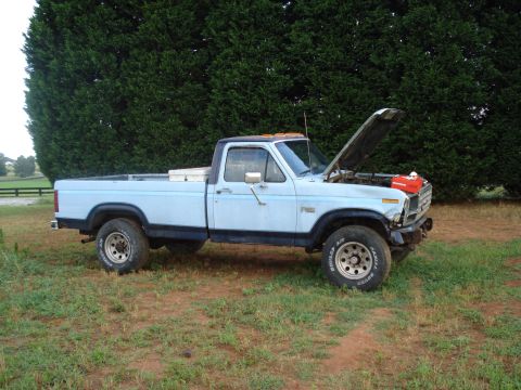 1984 Ford F-250 - A light blue pickup truck sits in a grassy area with its hood open, revealing the engine compartment.