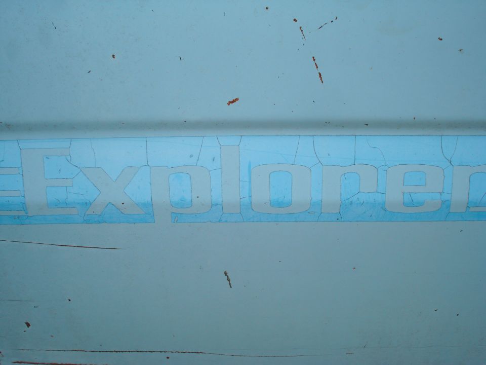 Close-up of a light blue vehicle panel with cracked white lettering spelling "Explorer"