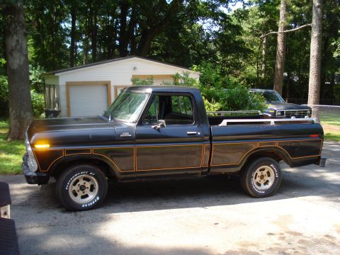 1984 Ford F-250 - A black Ford pickup truck with distinctive side trim is parked in front of a garage, with another vehicle behind it.